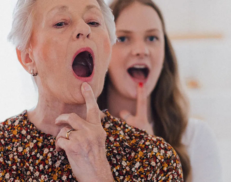 Patientin und Logopädin üben vor einem Spiegel