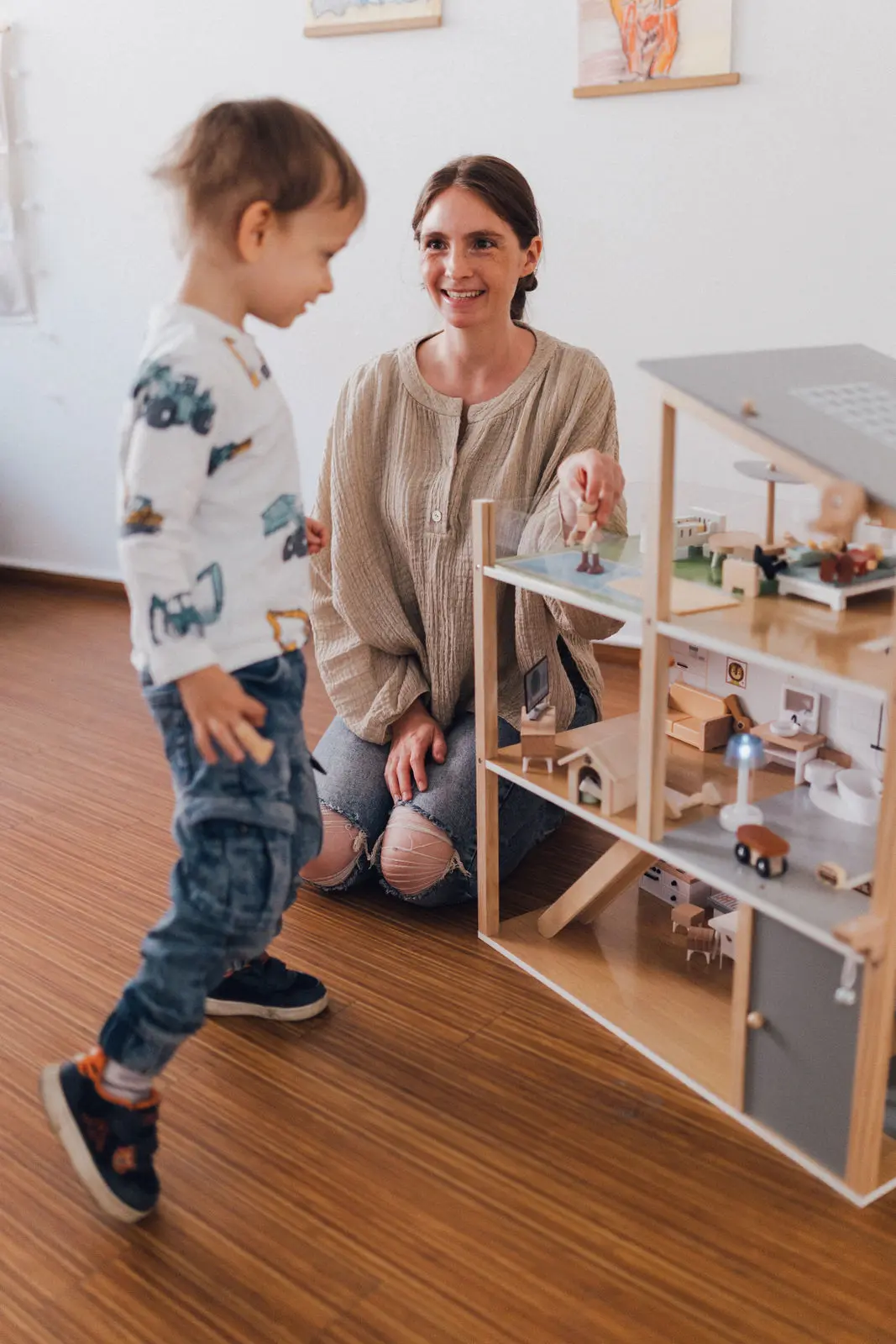 Kind mit Logopädin an einem Puppenhaus