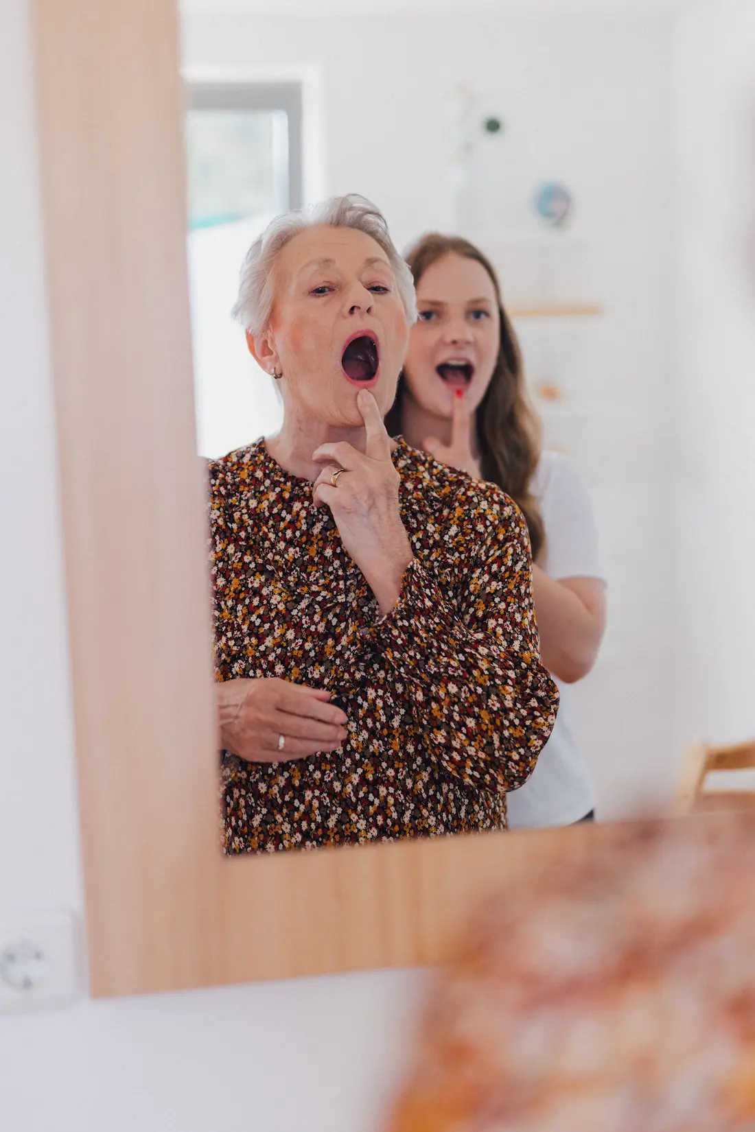 Frau und Logopädin machen Sprechstörungen vor einem Spiegel