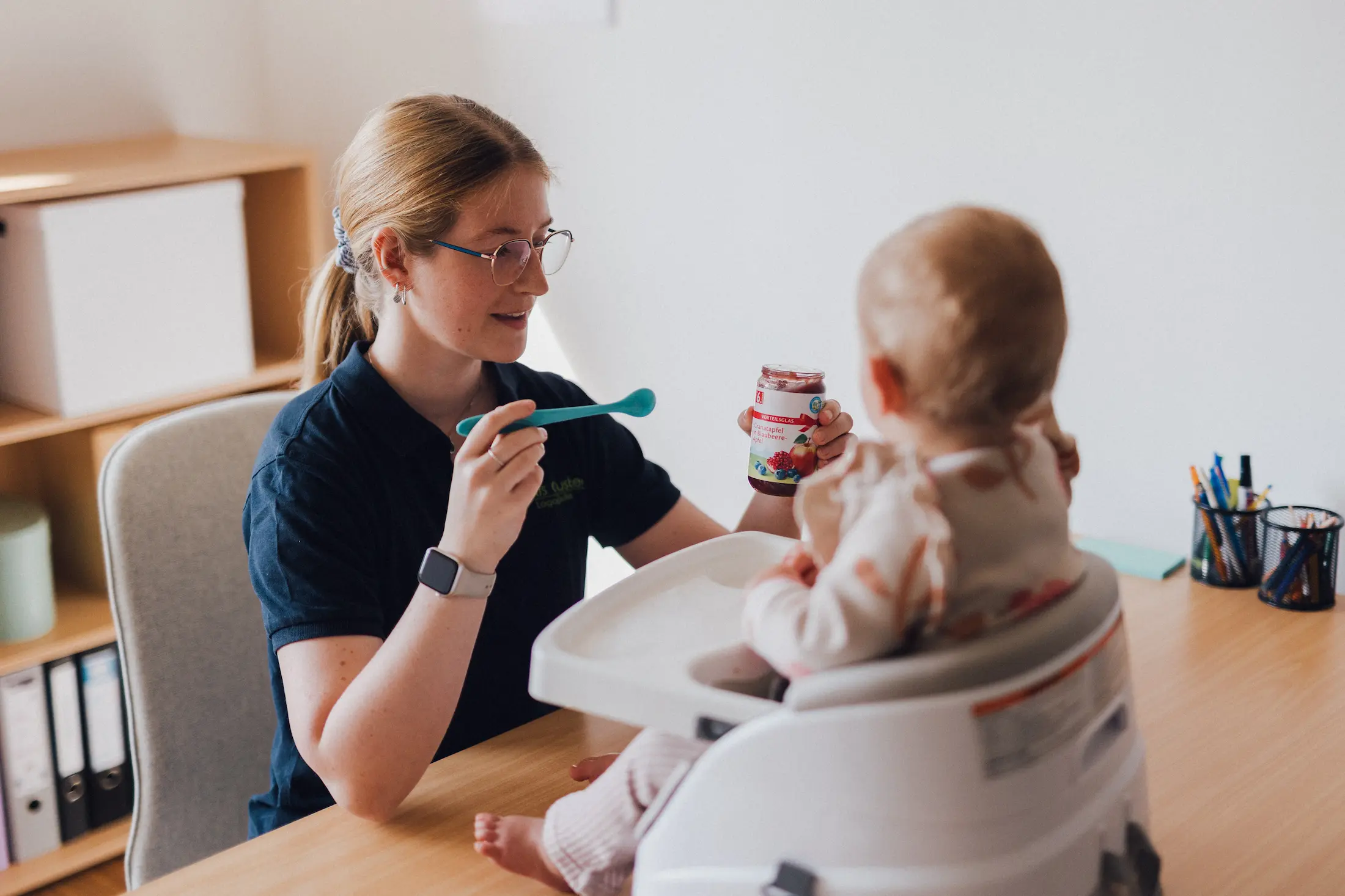Logopädin füttert ein Baby in einem Hochstuhl