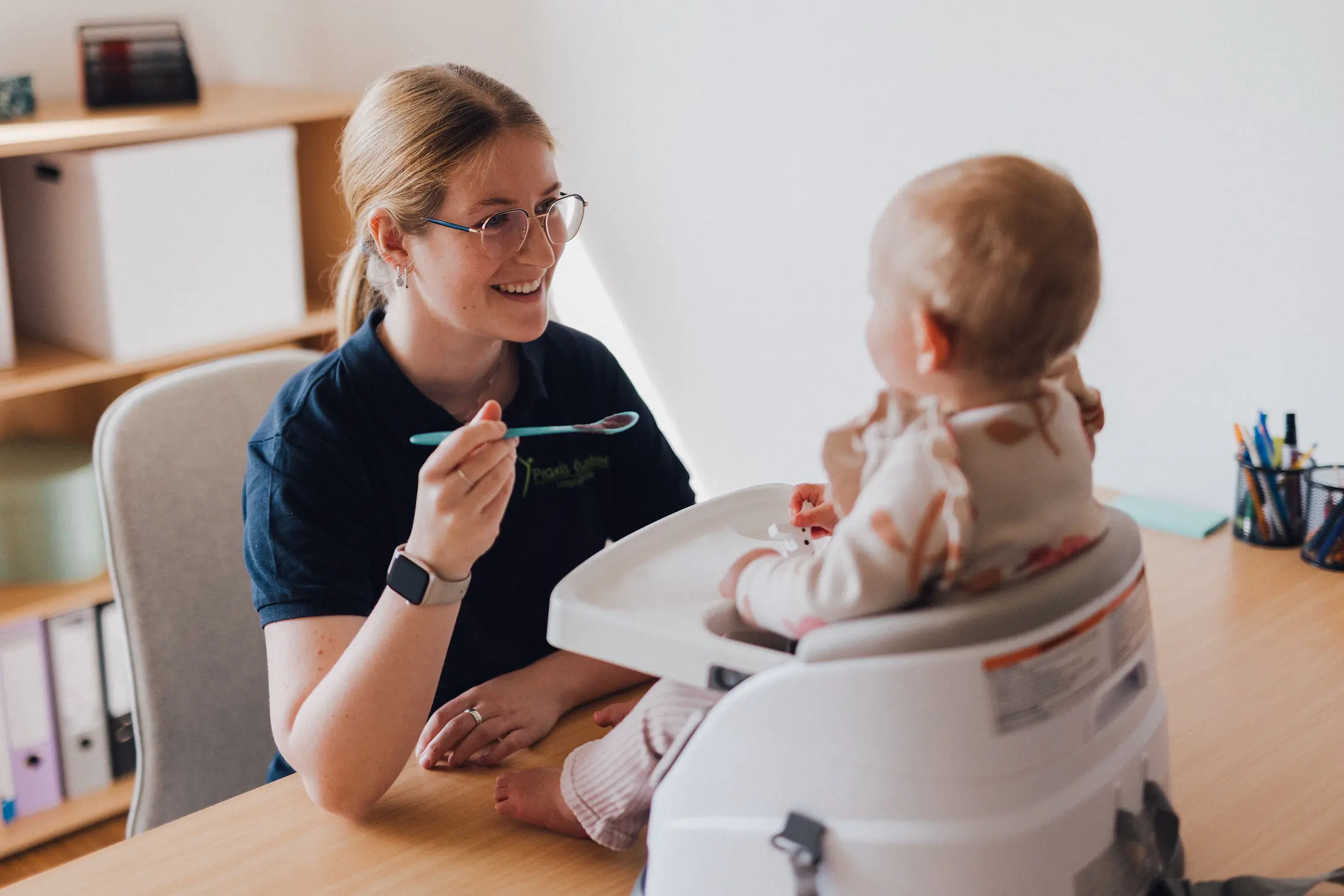 Logopädin lacht mit einem Baby in einem Hochstuhl
