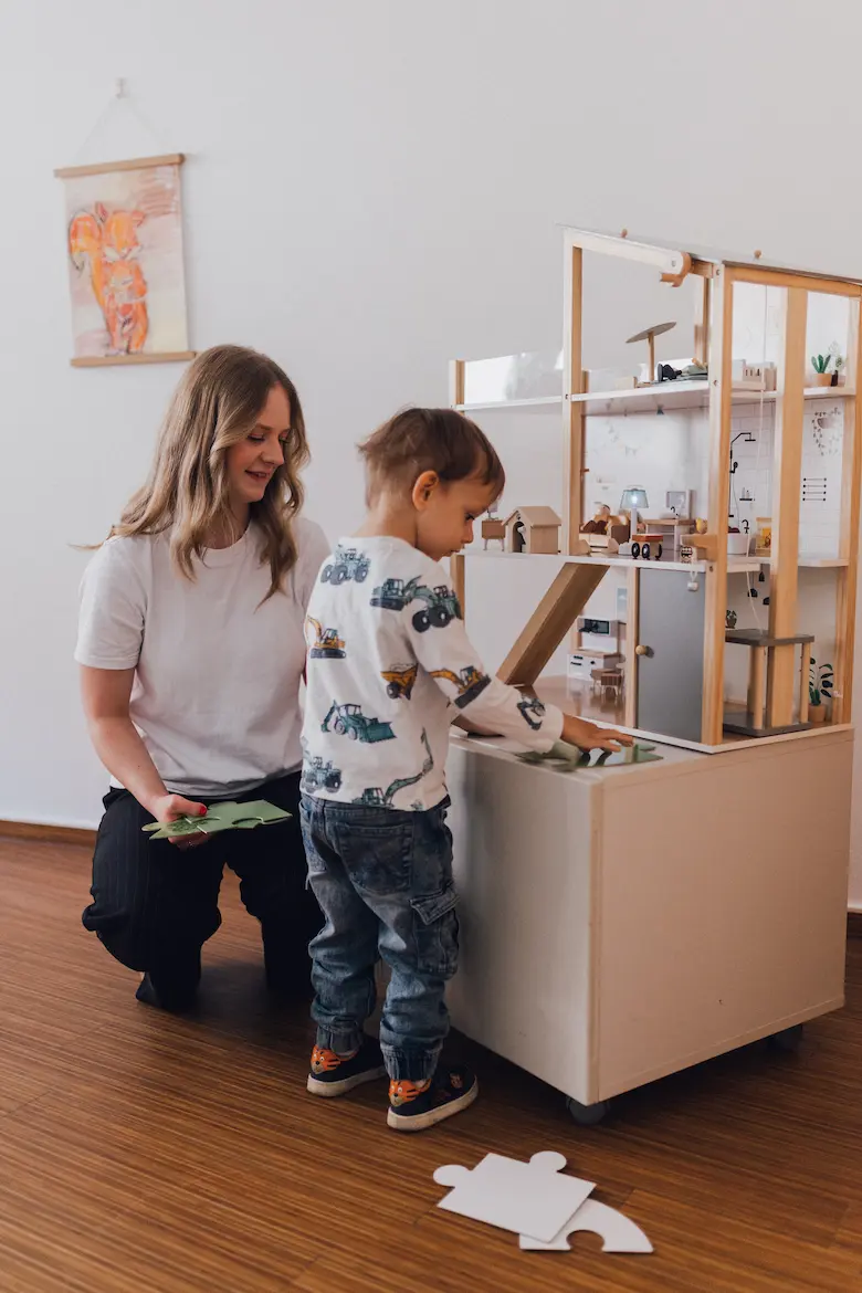Logopädin und Kind beschäftigen sich mit einem Puppenhaus