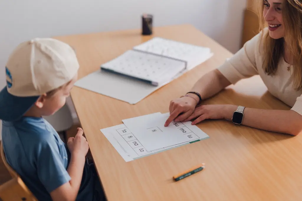 Frau erlärt einem Kind Buchstaben auf einem Blatt