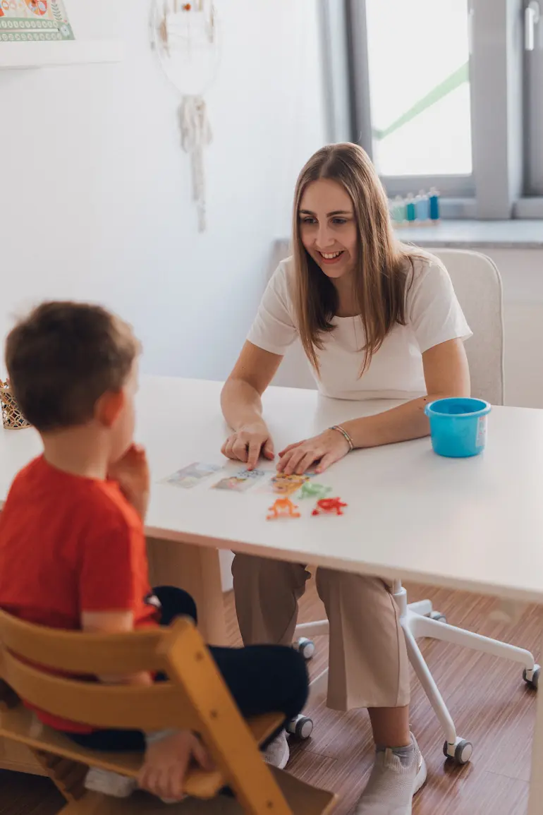 Kind und Logopädin spielen mit Bildkarten und Spielzeug-Fröschen