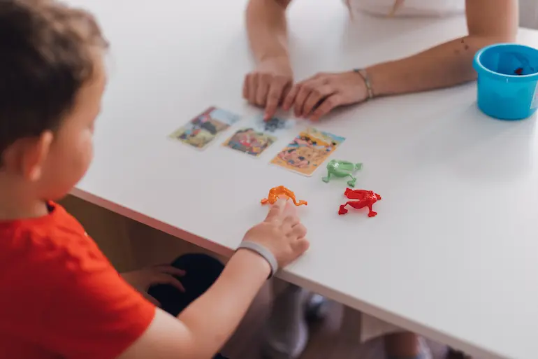 Kind und Logopädin spielen mit Bildkarten und Spielzeug-Fröschen