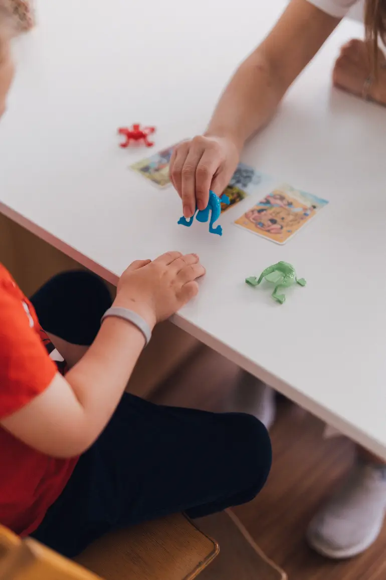 Kind und Logopädin spielen mit Bildkarten und Spielzeug-Fröschen