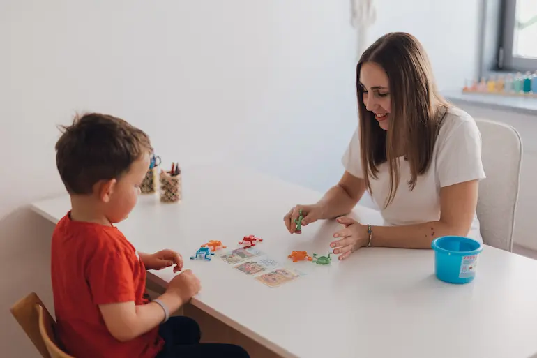 Kind und Logopädin spielen mit Bildkarten und Spielzeug-Fröschen